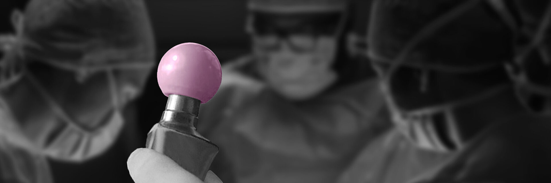 Close-up image of a surgeon holding a BIOLOX®delta ceramic femoral head implant, with three surgical team members in the background preparing for total hip arthroplasty. The image emphasizes the use of advanced ceramic biomaterials in orthopedic joint replacement procedures.